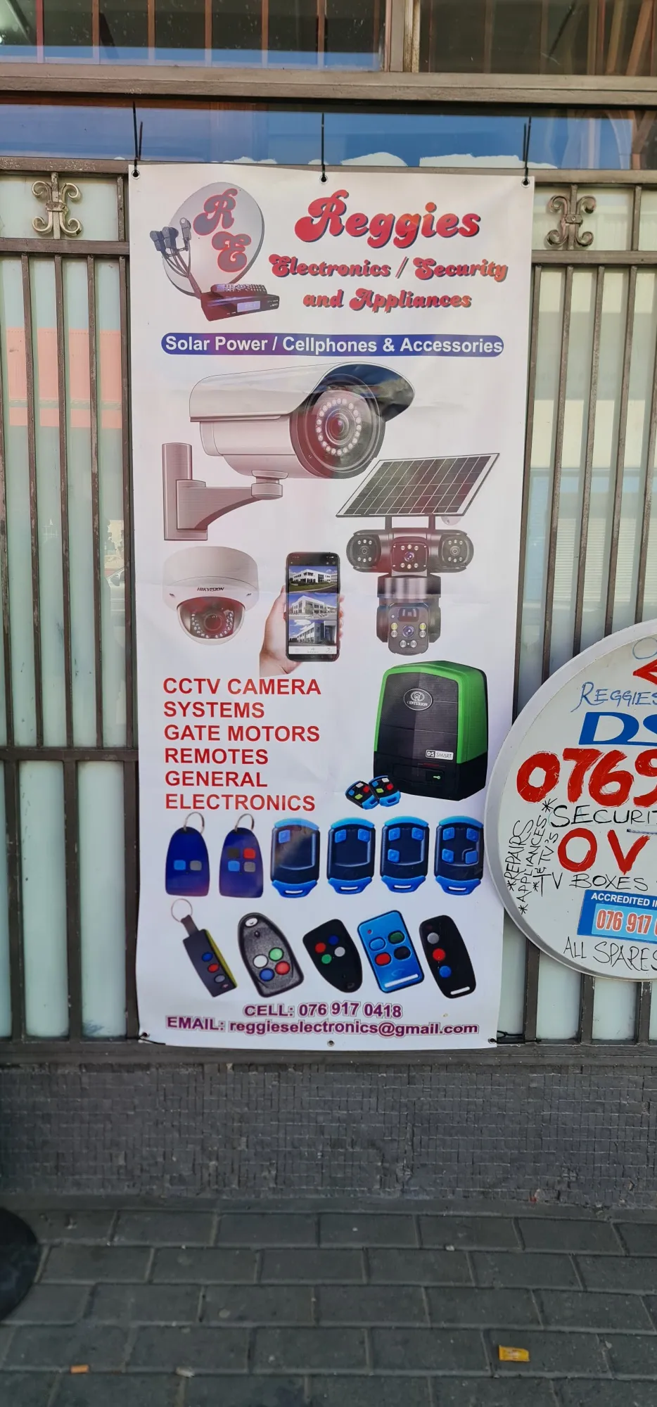 Printed outdoor PVC banner hung across a shopfront, advertising security cameras and electronics.