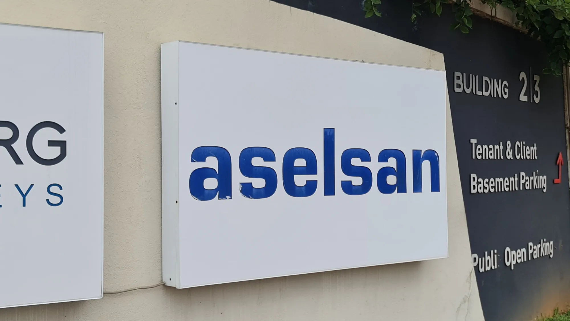 Wall-mounted illuminated panel sign with raised blue lettering on a building exterior.